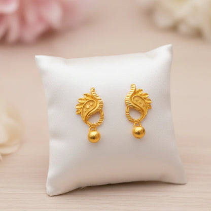 Gold plated manga mani earrings on a white cushion with a soft pink background