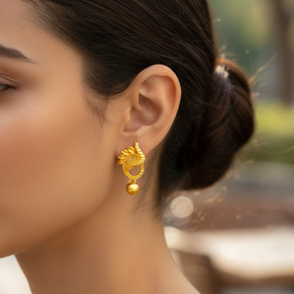 Close-up of a woman wearing a gold plated manga mani earring with a blurred outdoor background