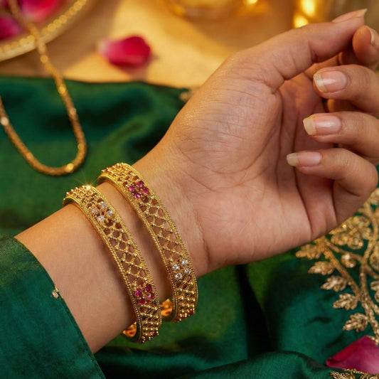 Gold plated bangles on a hand with a green saree in the background