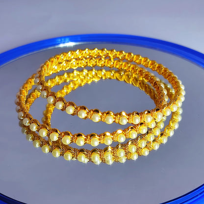 Set of gold plated and pearl beaded bracelets on a reflective surface