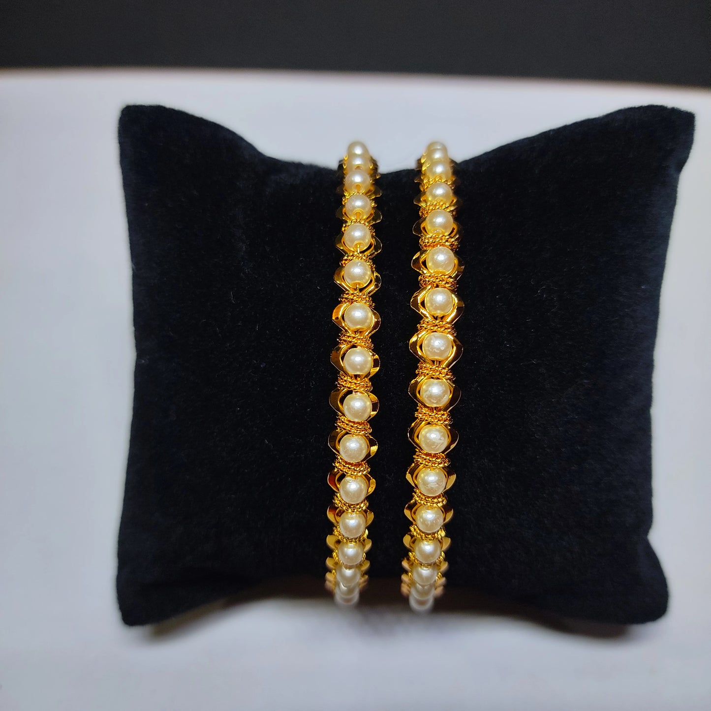 Two gold plated pearl beaded bangles on a black pillow