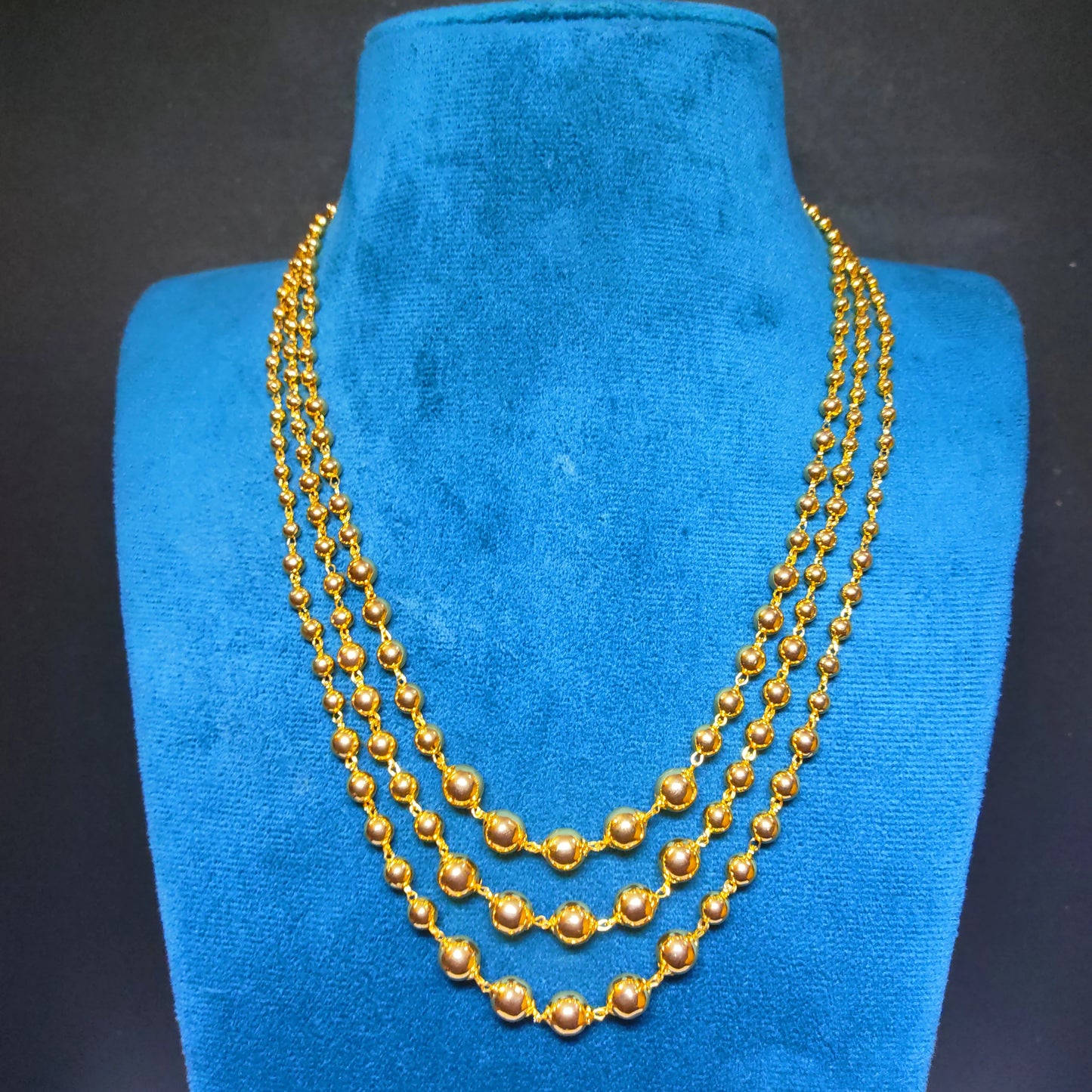 Gold plated 3 layered beaded necklace on a blue velvet stand