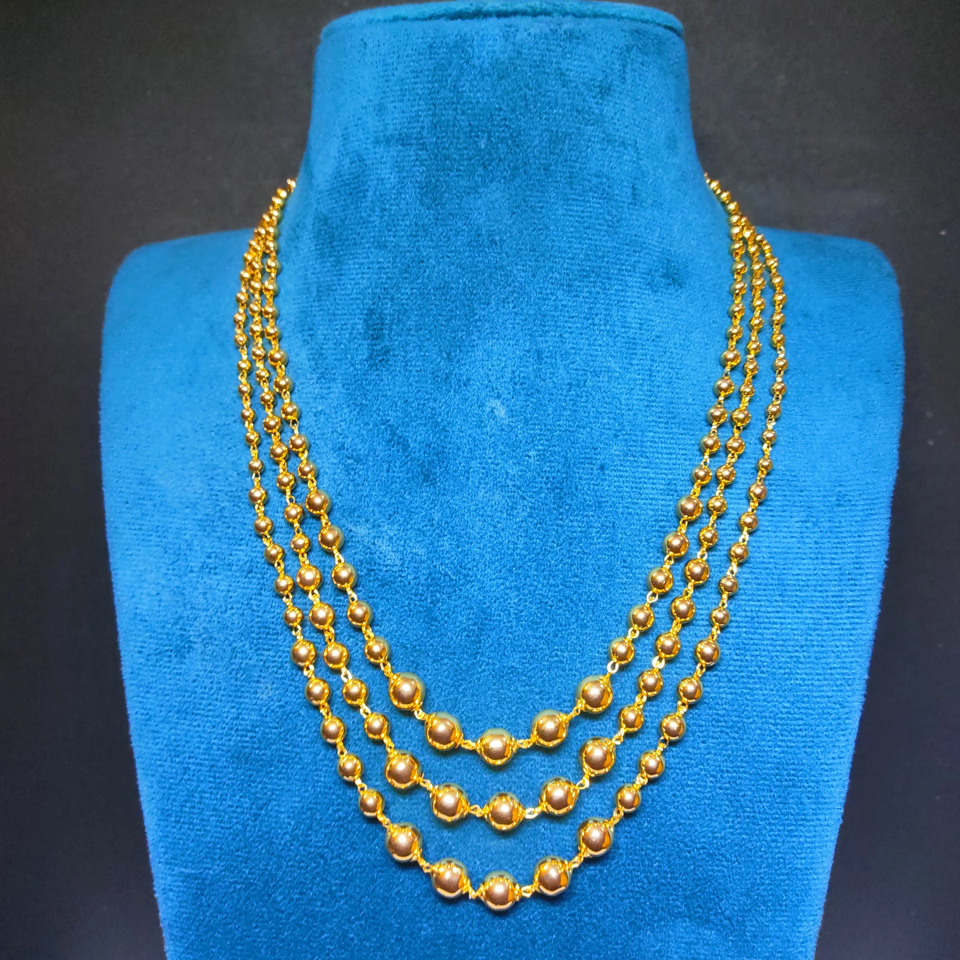 Gold plated 3 layered beaded necklace on a blue velvet stand