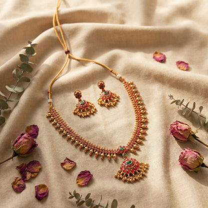 Ornate necklace and earrings on a beige fabric background with dried flowers and leaves.