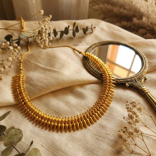 Gold plated necklace on a textured surface with dried flowers and a small mirror.