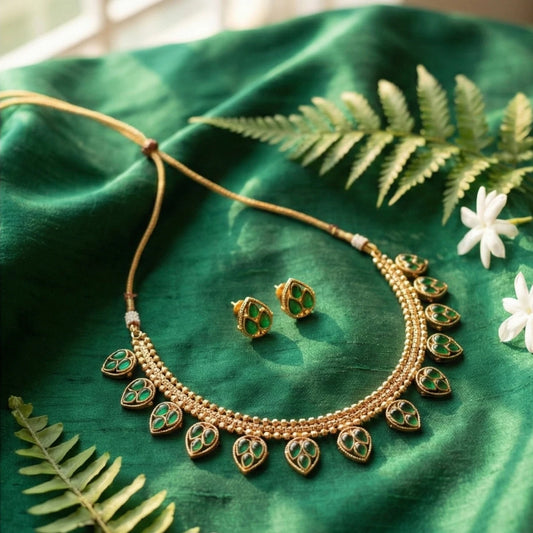 Gold toned necklace and earrings on a green fabric background with leaves and flowers.