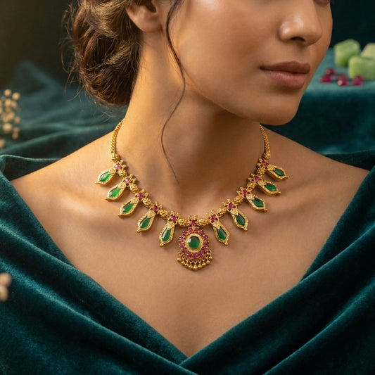 Woman wearing a gold plated Kerala Nagapadam Palakka necklace with green and red stones against a dark background