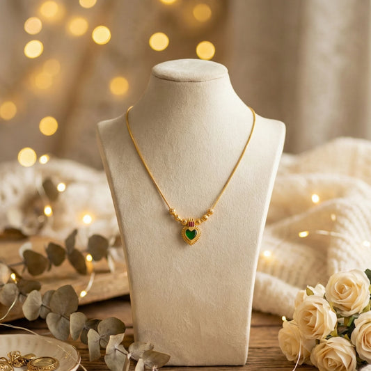 Gold plated necklace with a heart-shaped palakka pendant on a mannequin bust with decorative lights and flowers in the background