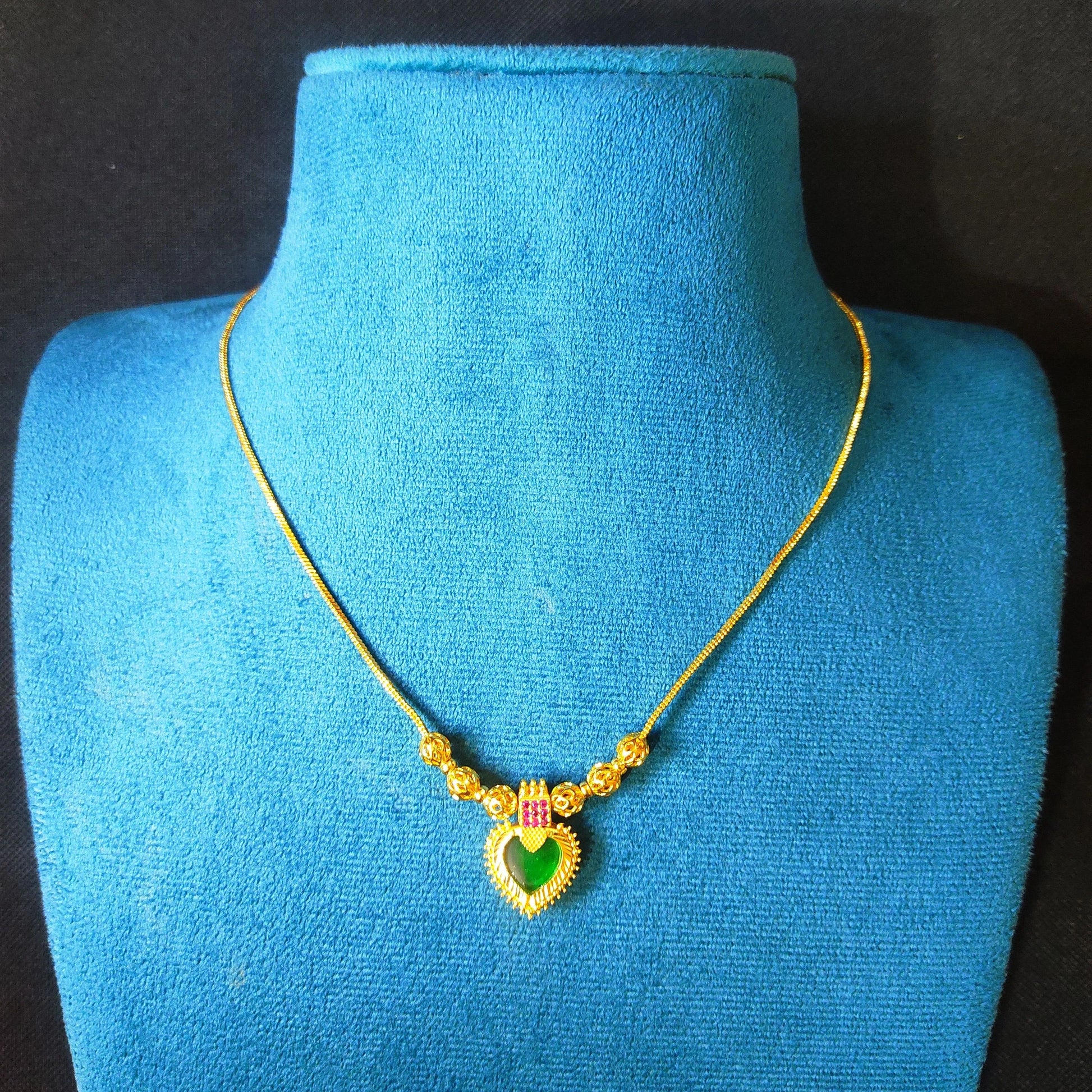 Gold plated necklace with a heart-shaped pendant on a blue mannequin