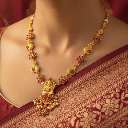 Gold toned necklace with red and green gemstones on a person wearing a maroon saree.