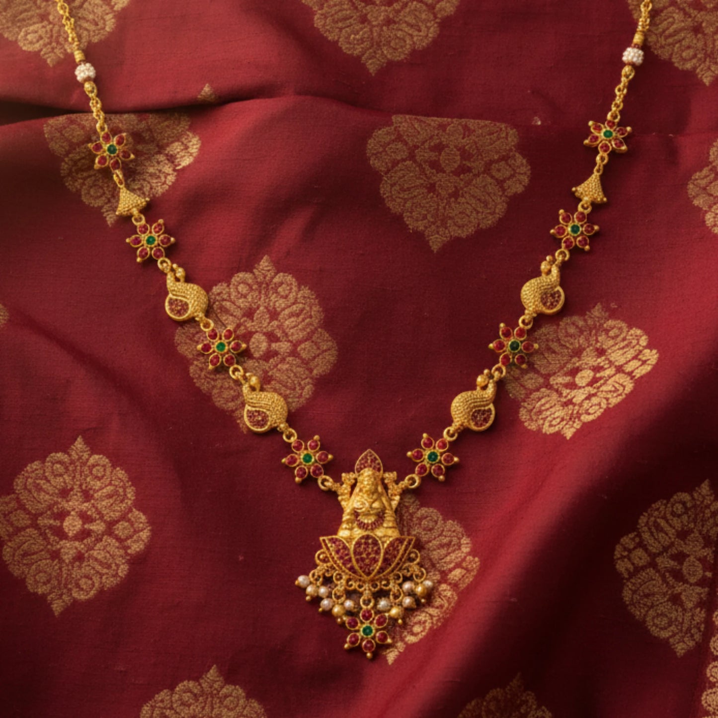Gold toned necklace with green gemstones on a red fabric background