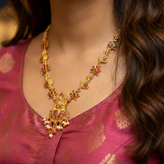 Gold toned necklace with gemstones on a person wearing a pink traditional outfit.