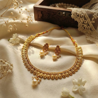 Gold toned necklace and earrings with pearls on a soft fabric background