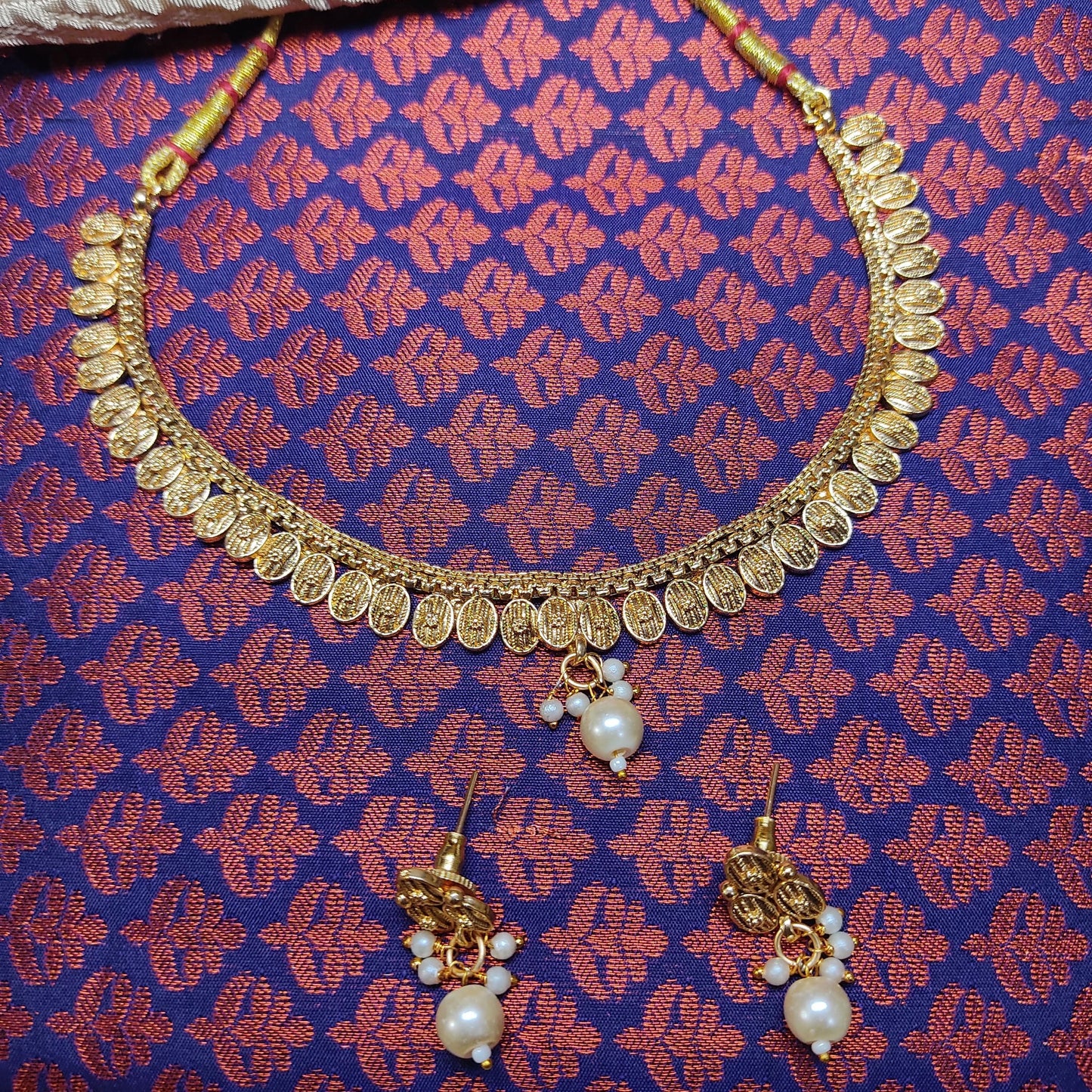 Gold toned necklace and earrings set on a patterned fabric background