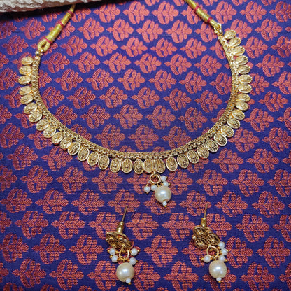 Gold toned necklace and earrings set on a patterned fabric background