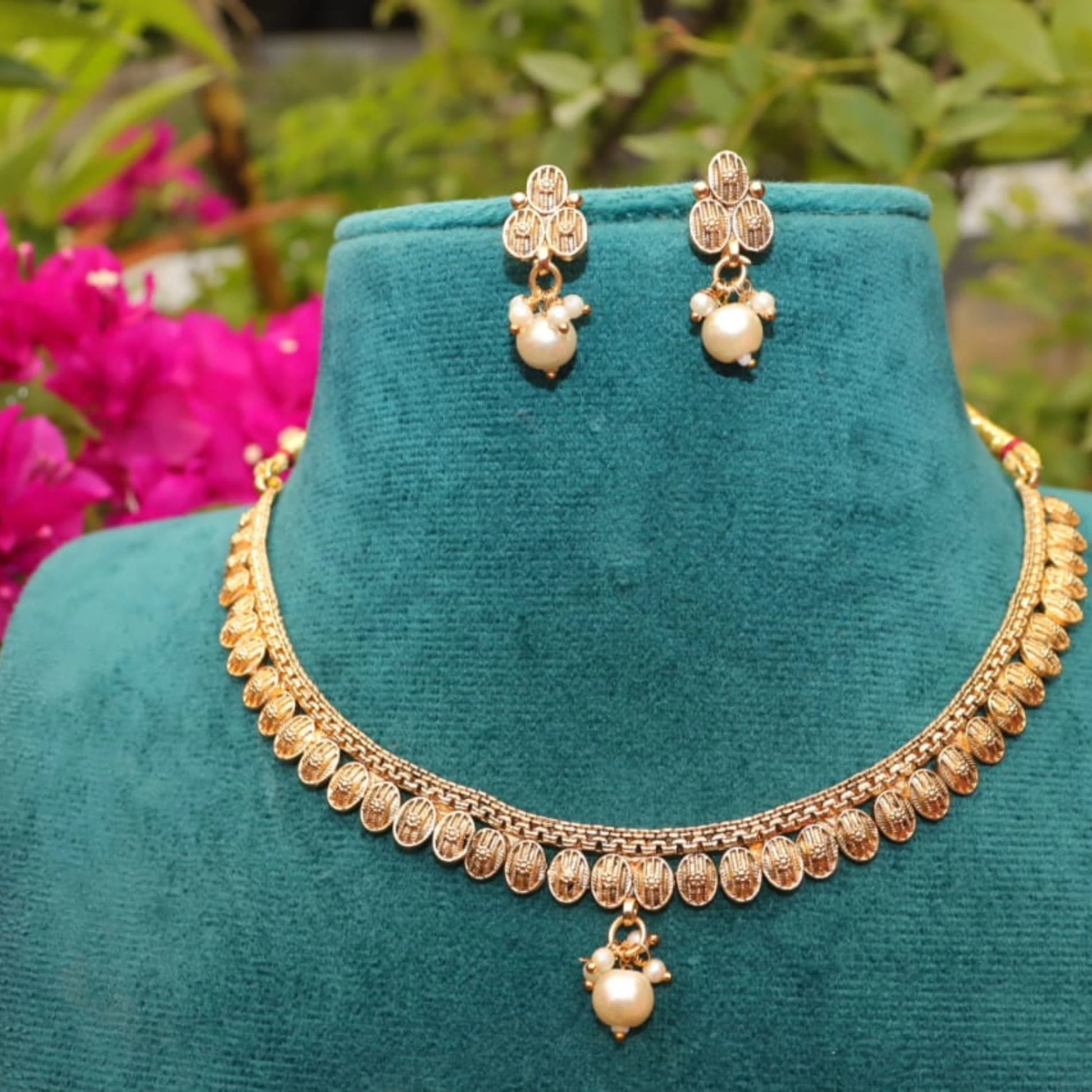 Gold toned necklace and earrings on a teal stand with flowers in the background