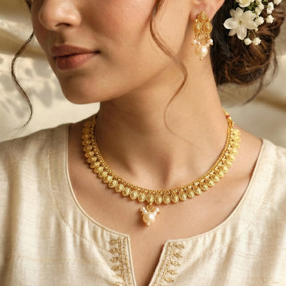 Woman wearing a gold toned necklace and earrings with a neutral background