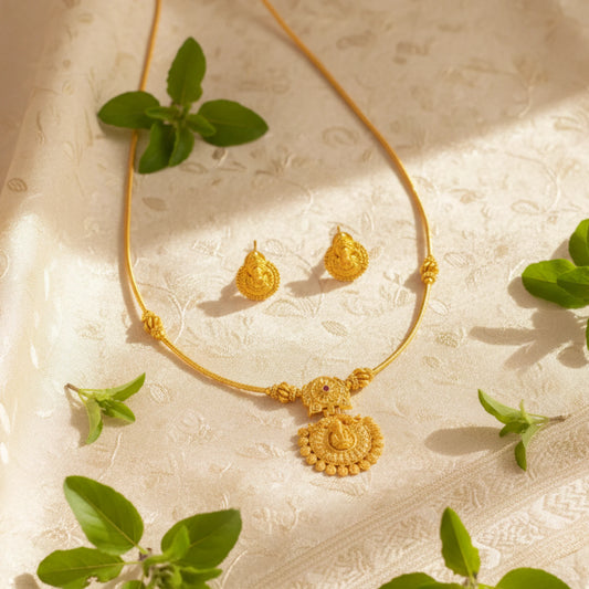 Antique Gold Finish necklace and earrings on a textured beige surface with green leaves.