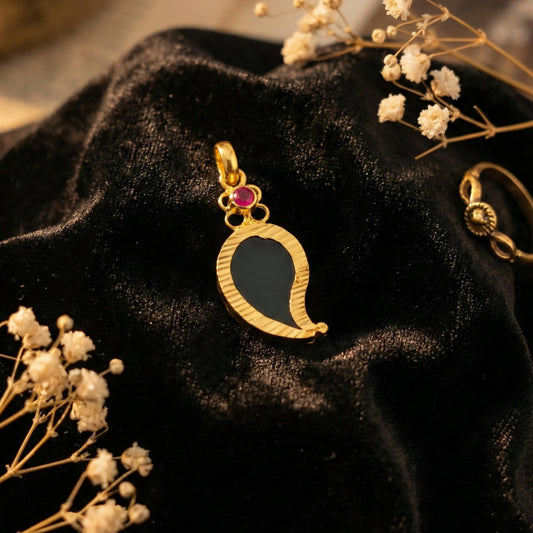 Gold plated Palakka pendant with a pink gemstone on a black fabric background with dried flowers.