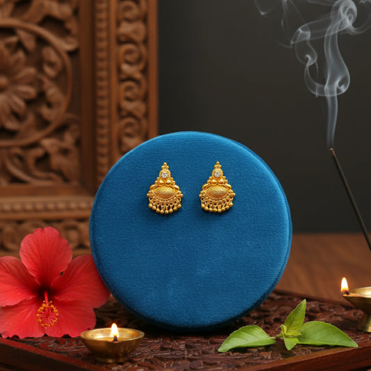 Gold plated earrings on a blue cushion with a red flower and incense stick in the background