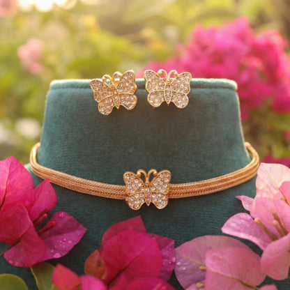 Gold toned Butterfly-themed jewelry set on a green velvet stand with pink flowers in the background