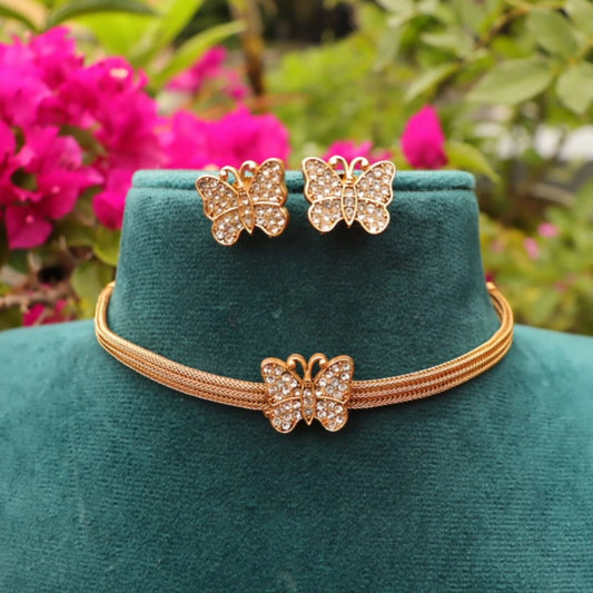 Butterfly-themed jewelry set on a green velvet stand with pink flowers in the background in the garden